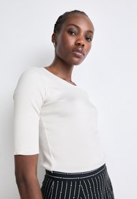 Lichtbeige getailleerde top met driekwart mouwen, ronde halslijn, zachte textuur, gecombineerd met een zwart-wit gestreepte high-waisted rok.