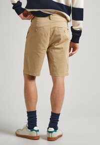 Pantalones cortos de algodón beige con un corte recto, que presentan dos bolsillos traseros, y combinados con zapatillas blancas y calcetines de canalé azul marino.
