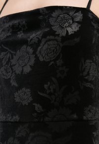 Svart fløyelsstoff med et ugjennomsiktig blomsterpattern i mørkere nyanser, som fremhever intrikate blomster- og bladdesign med en jevn tekstur.