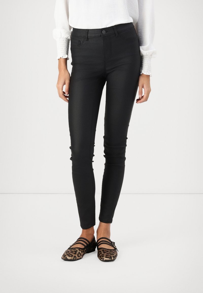 Jean skinny noir avec une taille haute, texture lisse et coutures minimales ; associé à des ballerines noires avec imprimé léopard et des brides.