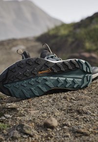 Zwarte en blauwe wandelschoenen met robuuste Continental rubberzolen die rusten op rotsachtig bergterrein.