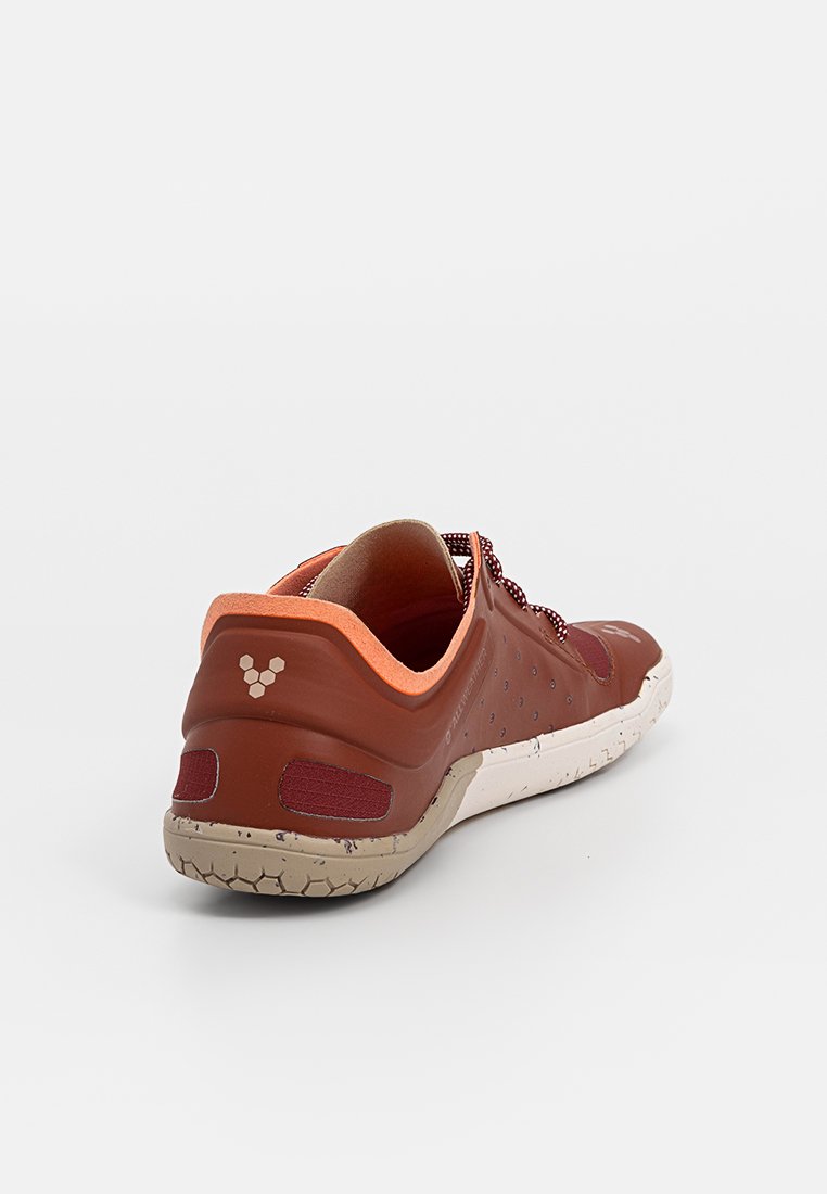Zapatilla deportiva marrón con un acento naranja, suela de goma texturizada y detalles de malla. Presenta una punta redondeada y un diseño de tacón plano en la parte trasera.