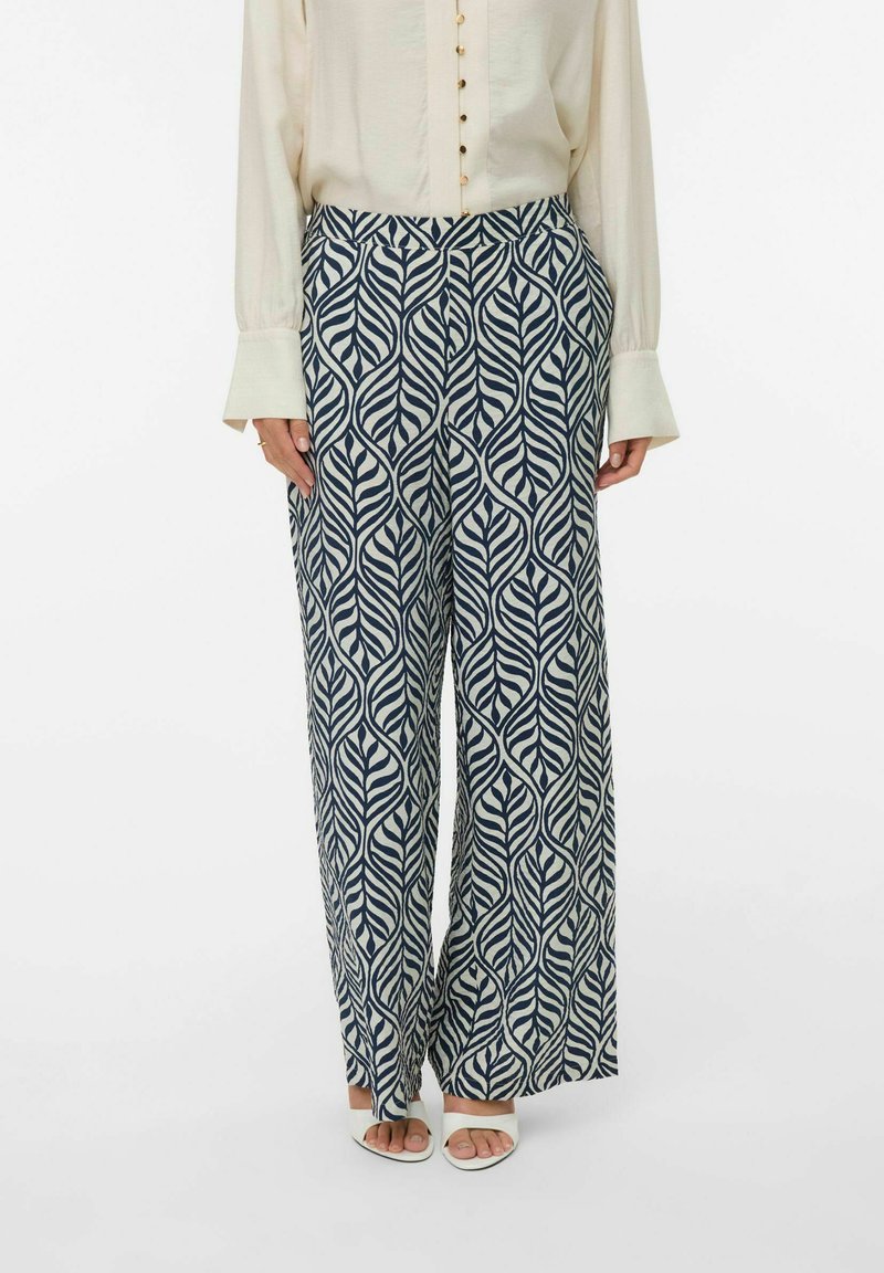 Pantalons larges en bleu marine et crème, présentant un motif de feuilles. Fabriqués en matériau léger, avec une taille élastique et des poches latérales.