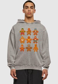 Sudadera gris con figuras de jengibre coloridas y de estilo caricaturesco que representan a varios superhéroes, mostradas de forma destacada en la parte delantera.