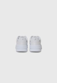 Zapatillas blancas con una parte superior de cuero suave, cuello acolchado y suela de goma texturizada. Presenta una marca mínima en el talón.