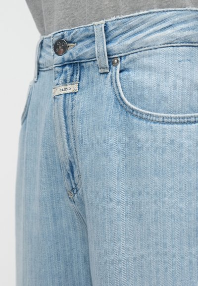 Jean en denim bleu clair avec un motif chevrons, doté d'une fermeture à bouton, de passants de ceinture, et d'une petite étiquette portant l'inscription "CLOSED".
