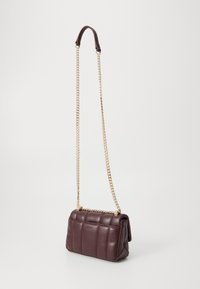 Bolso de mano de cuero acolchado marrón oscuro con correa de cadena dorada y almohadilla de hombro de cuero, apoyado contra un fondo blanco liso.