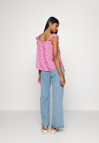 Top rosa com padrão floral e alças com babados, combinado com jeans de perna larga azul claro e sapatos de plataforma bege, visto de costas.