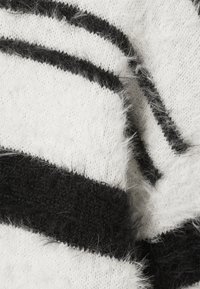 Gros plan sur un tissu tricoté doux et moelleux avec des rayures horizontales noires et blanches et des fibres texturées.