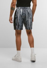 Sort og grå mønstrede shorts lavet af letvægtsstof, med en elastisk livrem og sidelommer. Båret med hvide sneakers og sokker.