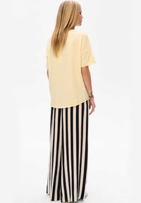 Gele oversized t-shirt gedragen met hoogwaisted zwart en crèmekleurige gestreepte wijde broek. Zacht materiaal, relaxte pasvorm en casual stijl.