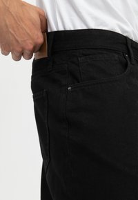Zwarte denim jeans met een gladde textuur, een aansluitend ontwerp en een leren patch op de tailleband. Bevat voor- en achterzakken.