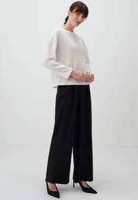 Witte, textuurrijke top met lange mouwen en een bloemenpatroon, gecombineerd met hoge zwarte wijde pantalon en zwarte puntige hakken.