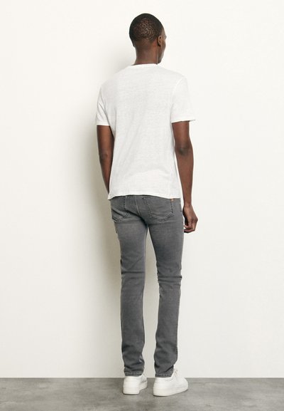 Hvit t-skjorte med korte ermer og rund hals, kombinert med slim-fit gråjeans, fullført med hvite joggesko; glatt stofftekstur er synlig.