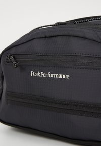Black fabric bag with textured surface, featuring a front zipper pocket, peak performance logo in white, and reinforced stitching details.