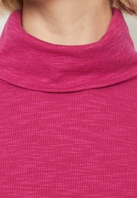 Rosa ribbad polo-tröja med hög krage. Tyget har en strukturerad, något melerad yta med subtila tonalitetsvariationer.