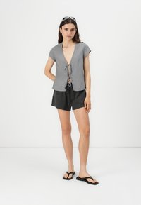 Gray striped short-sleeve top with a V-neck and front tie detail, paired with black shorts and black flip-flops, against a plain background.