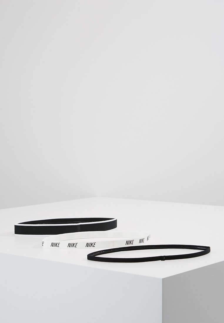 Dos cintas para la cabeza de Nike: una negra con una textura lisa, una blanca con letras negras, ambas con un diseño simple y plano.