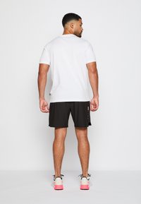 Camiseta blanca de manga corta combinada con pantalones cortos deportivos negros. Cuenta con un diseño minimalista, tejido suave y acentos reflectantes de luz.