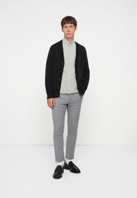 Čierny kardigán s gombíkmi, pod ním pruhovaná šedá košeľa, šedé slim-fit nohavice a čierne poltopánky. Jednoduchý, moderný dizajn a farebná schéma.
