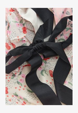 Czarna wstążka grosgrain związana w kokardę na tkaninie w kwiaty z czerwonymi wiśniami, różowymi kwiatami, zielonymi liśćmi i małymi czerwonymi serduszkami.