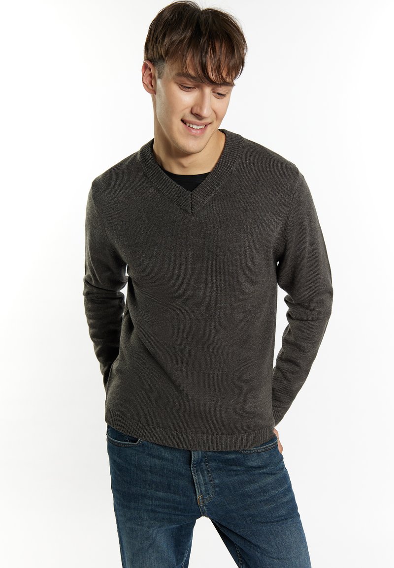 Donkergrijs v-hals sweater met ribbelmanchetten en -zoom, gemaakt van gestructureerd brei-echt, gedragen over een zwart shirt, gecombineerd met blauwe jeans.