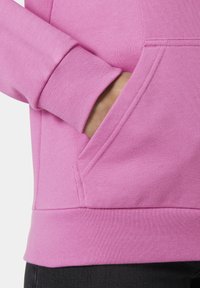 Sudadera rosa con una textura suave, que presenta un bolsillo canguro y puños acanalados. El dobladillo es ligeramente más largo, ofreciendo un ajuste relajado.