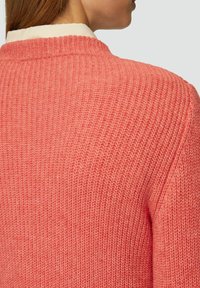 Gestrickter Pullover in Korallenfarbe, mit einem strukturierten Rippmuster und hohem Kragen. Die Rückansicht zeigt ein nahtloses Design und weichen Stoff.