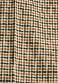 Textil med ett hundtandsmönster som har brunt, orange och svart mot en krämfärgad bakgrund. Materialet ser texturerat och vävt ut.