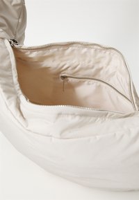 Bolso acolchado beige con cierre de cremallera, que presenta un forro interior suave y un pequeño bolsillo con cremallera en el interior.