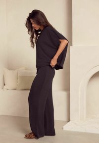 Mørkegrå loungewear sæt bestående af en løstsiddende top med brede ærmer og højtaljede, vide bukser, parret med tøfler i dyreprint.