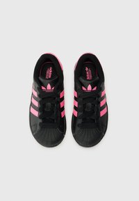 Sorte sneakers med tre rosa striper, gummihælkappe og sorte lisser. Teksturert materiale med logodetalj på innersålen.