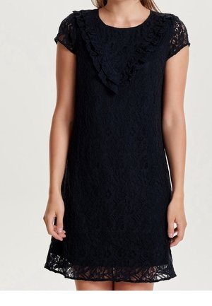 Schwarzes Spitzenkleid mit kurzen Ärmeln und einer Rüschendetail in V-Form auf der Brust, knielang, getragen von einer Person, die vor einem schlichten Hintergrund steht.