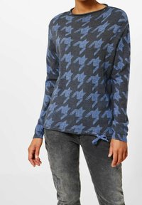 Stickad tröja i mörkgrått med ljusblått houndstooth-mönster; rund halsringning; långa ärmar; sidofäste vid nederdelen.