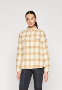 Camicia di flanella a quadri gialli con linee arancioni e blu, dotata di chiusura a bottoni sul davanti e due tasche sul petto. Maniche lunghe con polsini a bottoni.