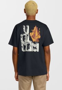 T-shirt noir avec un grand graphisme au dos portant le texte "VOLCOM" et un motif en forme de diamant multicolore. Matière en coton.