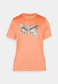 Orange Nike T-shirt med grafisk print, der viser øjne og tale-bobler. Kortærmet, rund halsudskæring, glat tekstur, atletisk pasform.