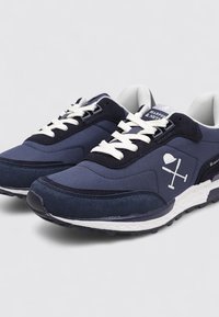 Zapatillas azul marino con materiales de malla y ante, cordones blancos y acentos grises en contraste. Presenta un logo con un diseño en el costado.