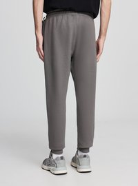 Szare spodnie dresowe ze zwężanymi nogawkami, elastycznym paskiem w talii oraz ściągaczami przy kostkach. Wykonane z miękkiego materiału, posiadają boczne kieszenie i minimalistyczny design.
