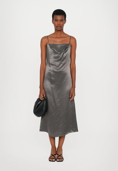 Gray satin spaghetti strap dress with a draped neckline, falling to mid-calf, paired with a black padded handbag and strappy sandals.