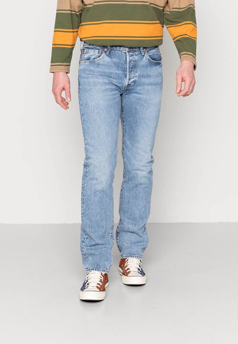 Ljust blå denimjeans med rak passform, femfickorsdesign och blekt textur. Bärs med flerfärdade sneakers och en randig långärmad tröja.
