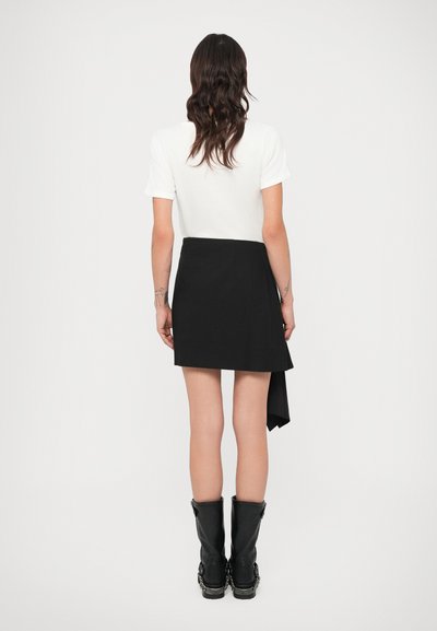 Čierna minisukňa s asymetrickým lemom, vyrobená z hladkej tkaniny, v kombinácii s bielym tričkom a čiernymi čižmami po kolená.