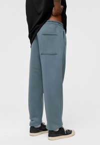 Lichtblauwe sweatpants met een relaxed fit, elastische tailleband en een enkele achterzak. Draag ze met zwarte sneakers en een losse zwarte shirt.