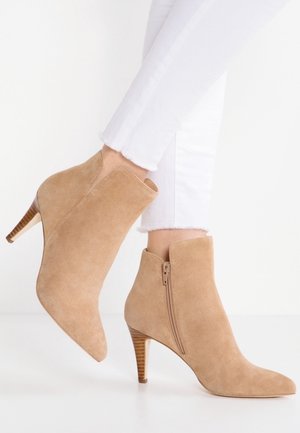 Beige suède enkellaarsjes met zijrits en houten blokhakken, gedragen met witte cropped broeken.