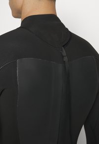 Muta nera con un design liscio e aderente. Presenta una texture opaca, cuciture senza soluzione di continuità e una cerniera sul retro con un anello in tessuto per un facile indossarla.