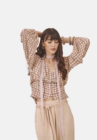 Blusa corta de color rosa claro con un patr�ón de cuadros, mangas acampanadas, botones frontales y acentos de cinta. Combinada con pantalones de talle alto beige.
