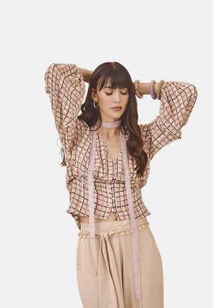 Blusa corta de color rosa claro con un patrón de cuadros, mangas acampanadas, botones frontales y acentos de cinta. Combinada con pantalones de talle alto beige.