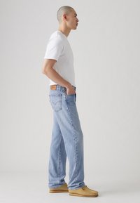 Lyseblå, løstsittende jeans med rette ben, en brun lærpatch på livlinjen, kombinert med en hvit t-skjorte med korte ermer og beige sko.