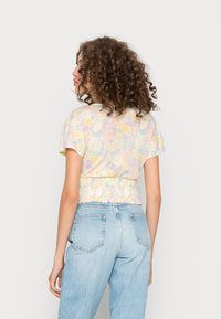 Tætsiddende cropped top lavet af letvægts, struktureret stof med et pastelblomstermønster, der har kortærmer og en rynket kant.