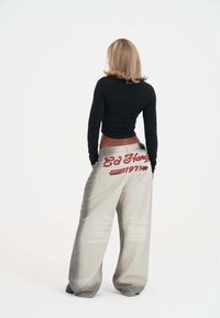 Top negro de manga larga con diseño ajustado; jeans de pierna ancha gris claro con texto bordado en rojo en el bolsillo trasero.